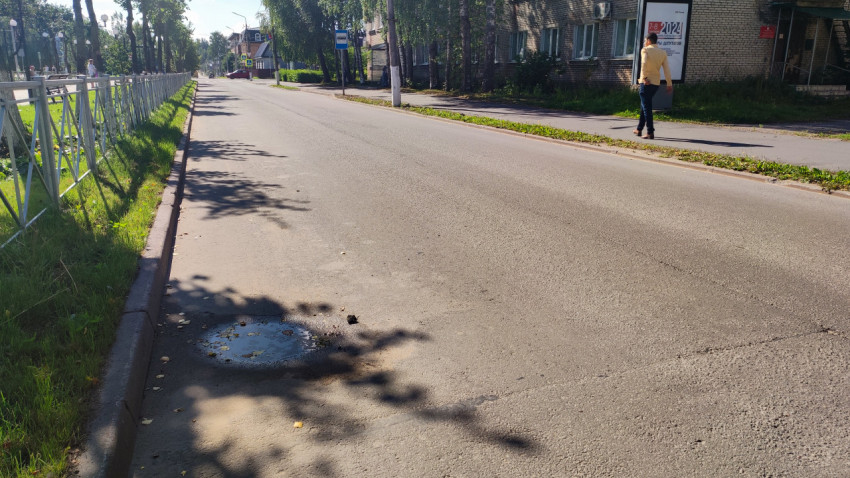 Лужа на асфальтовой дороге у тротуара и кирпичного здания с большим рекламным щитом