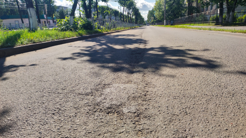 Дорога с тенями от деревьев и ограждениями вдоль тротуаров