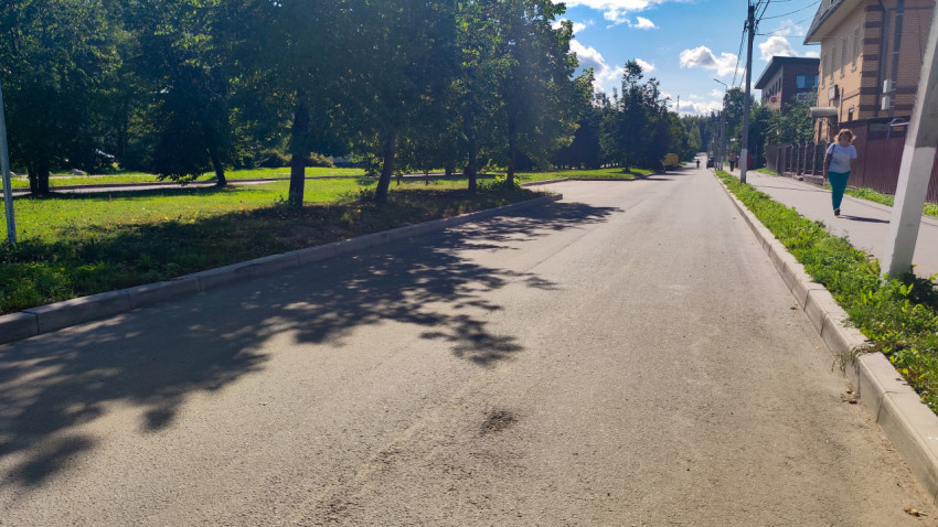 Тихая улица с тротуаром, деревьями и пешеходом у кирпичного здания