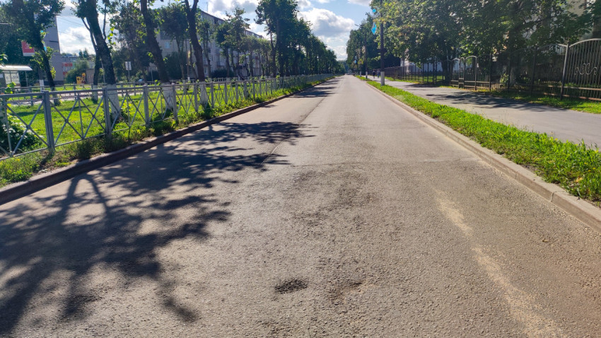 Пустая городская улица с асфальтовой дорогой, ограждениями и тенями деревьев