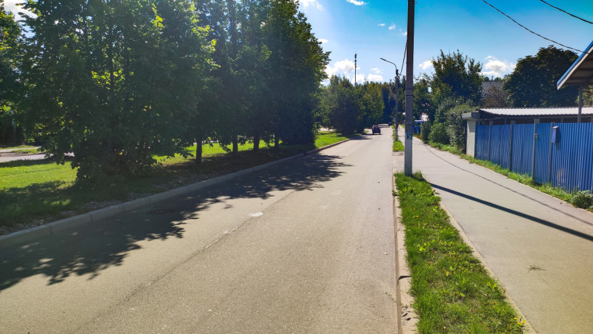 Асфальтированная улица с тротуаром, бордюром, опорой освещения и забором из профлиста