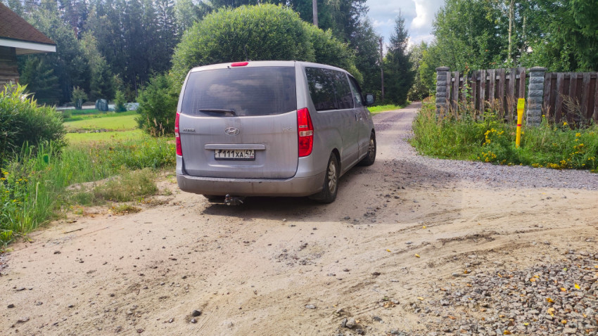 Серебристый минивэн на повороте грунтовой дороги у въездных ворот