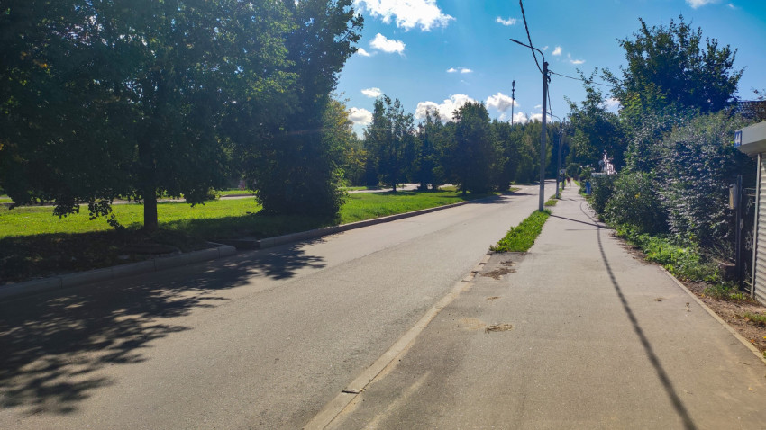 Дорога и тротуар у зелёной зоны с деревьями, фонарями и воздушными проводами