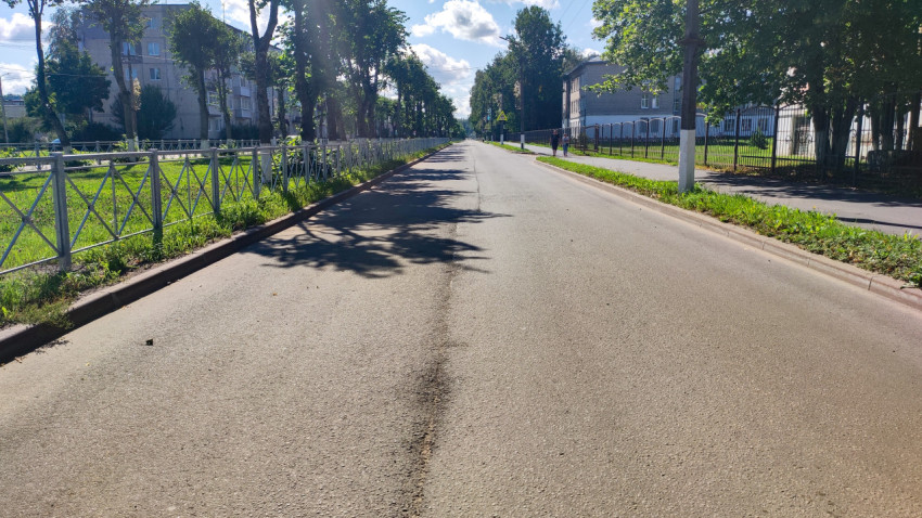 Прямая городская дорога с тротуаром, ограждениями и пешеходами вдоль квартала