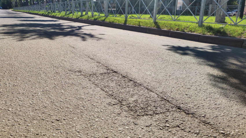 Крупный план асфальта со швом и заплаткой рядом с ограждением и травой