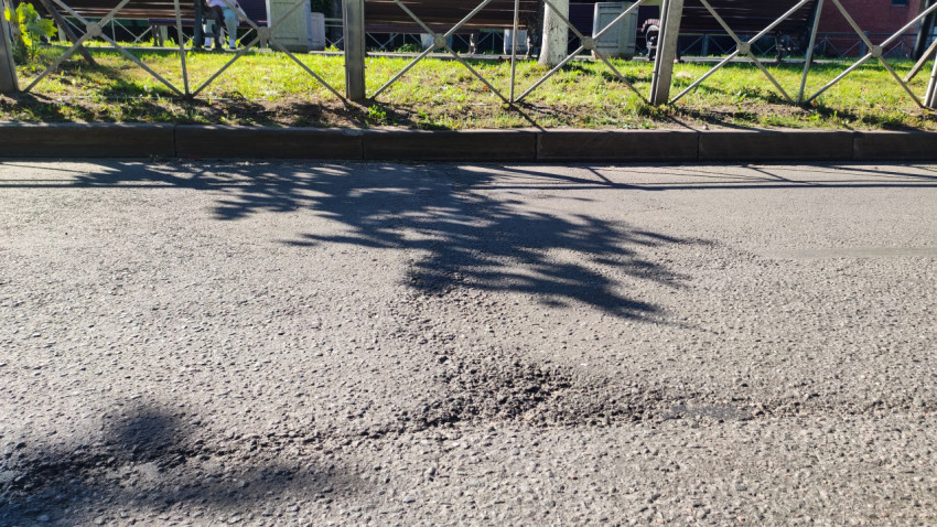 Повреждённый участок асфальта с крошкой и неровностями у края дороги