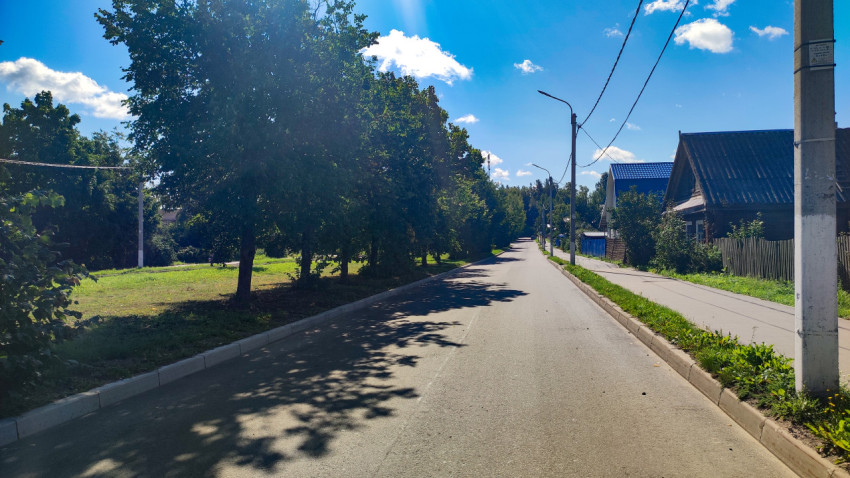 Прямая улица с асфальтом, тротуаром и деревьями, ведущая через частный сектор