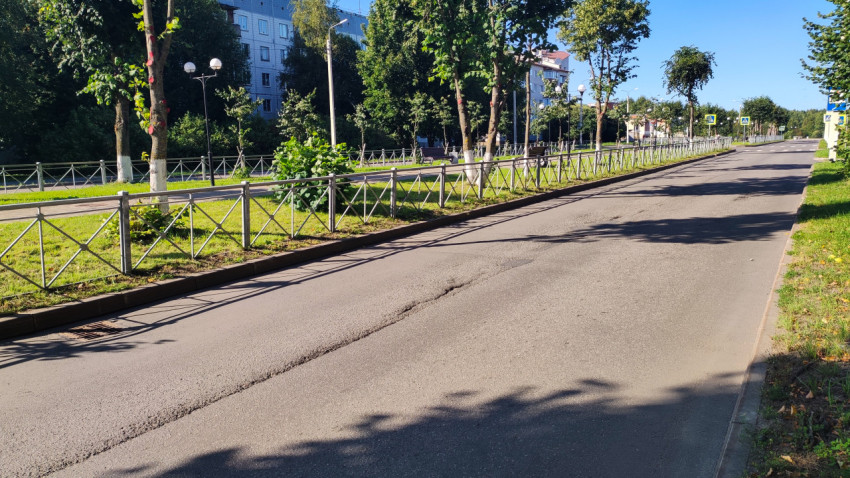 Небольшая яма на асфальте проезжей части рядом с газоном и тротуаром