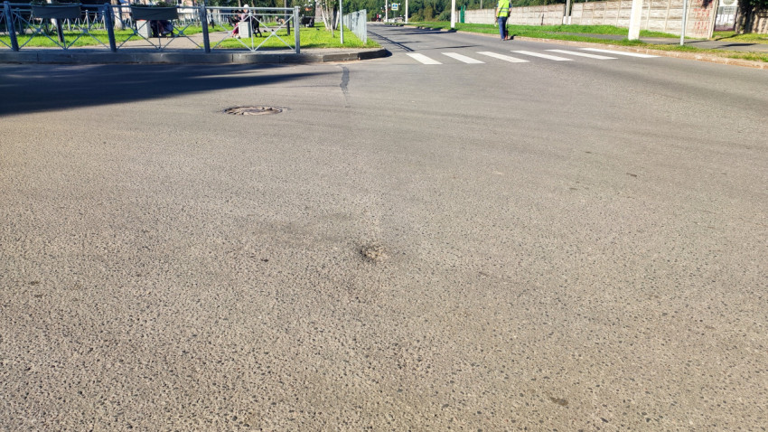 Низкий ракурс на асфальт с люком и трещиной рядом с перекрёстком