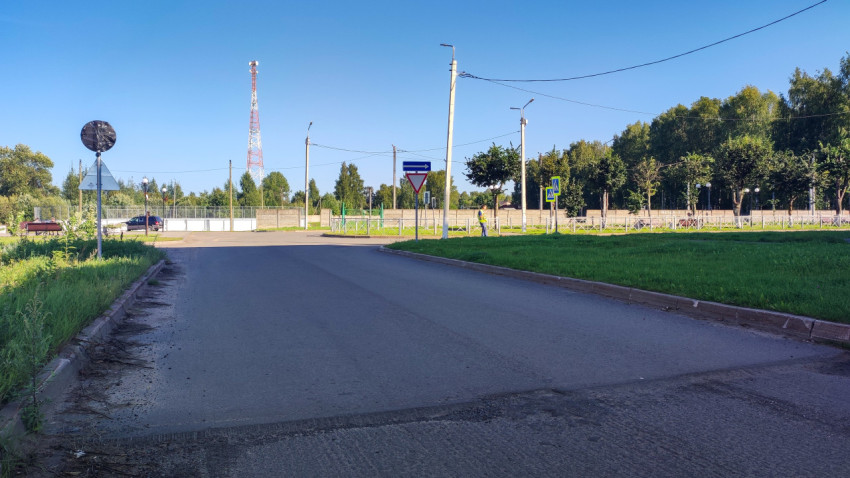 Пустая дорога к перекрёстку с дорожными знаками, опорами и зелёной обочиной в солнечную погоду