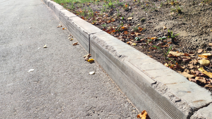 Кромка асфальта у бордюра с трещиной и сырой землёй в придорожной полосе