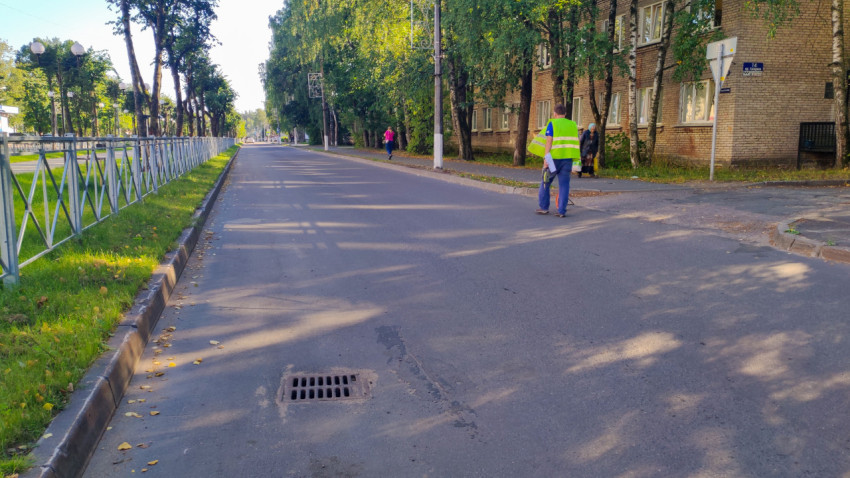 Ливневая решётка в асфальте на краю улицы рядом с тротуаром и проходящими людьми