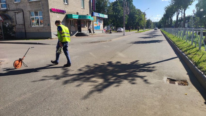 Рабочий в жилете переходит улицу с инструментом на фоне магазина и дорожных знаков