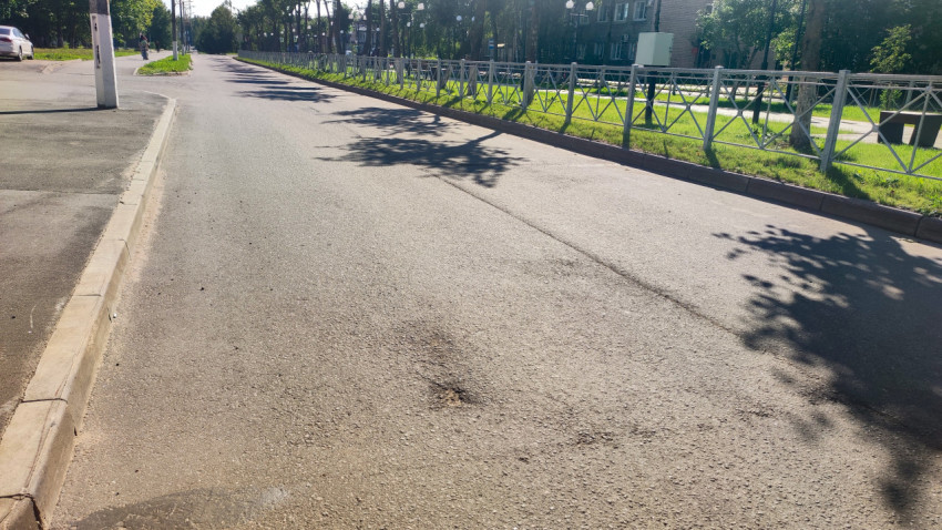 Длинная перспектива улицы с ограждением, деревьями и пятнами ремонта на асфальте