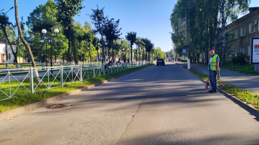 Дорожный специалист в сигнальном жилете стоит у обочины с измерительным колесом и штативом