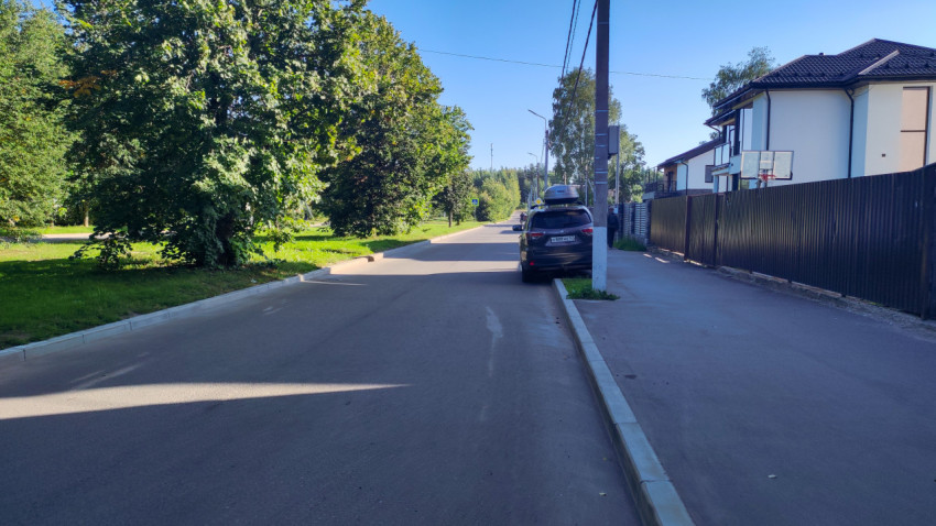 Тихая улица с припаркованным внедорожником у бордюра и тротуаром вдоль заборов частных домов