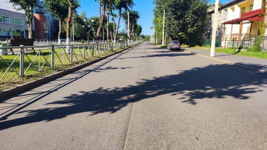 Тихая улица с пустой проезжей частью, ограждением и скамейками у деревьев