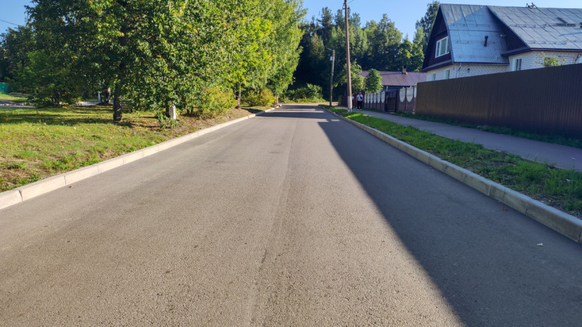 Прямая дорога с тротуаром, ограждением, деревьями и людьми вдалеке
