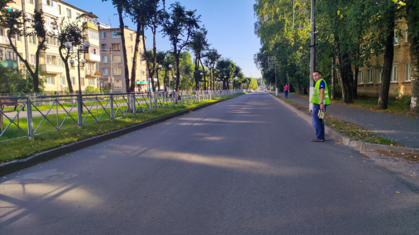 Специалист в жилете стоит у обочины с измерительным инструментом, проверяя состояние асфальта