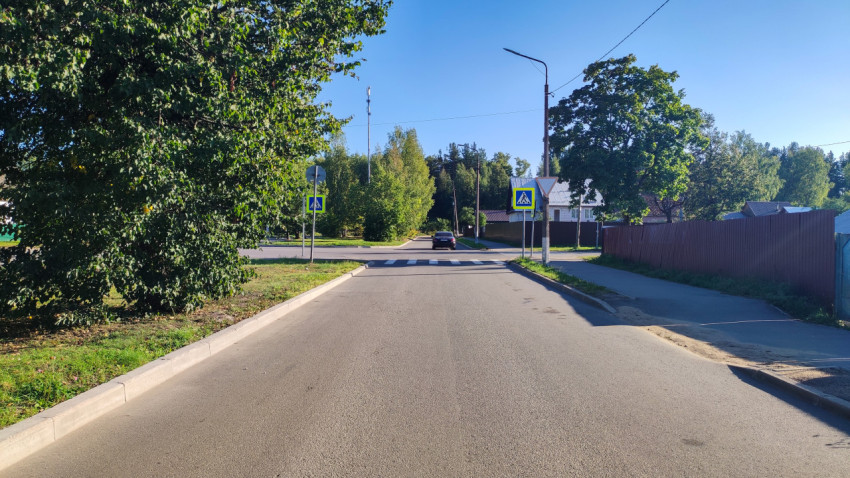Пешеходный переход со знаками на спокойной улице среди деревьев и заборов