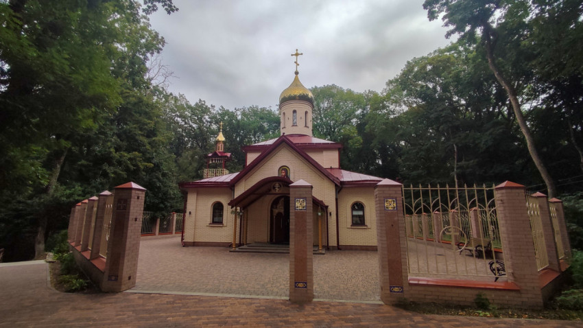 Православный храм с золотым куполом и оградой на фоне леса