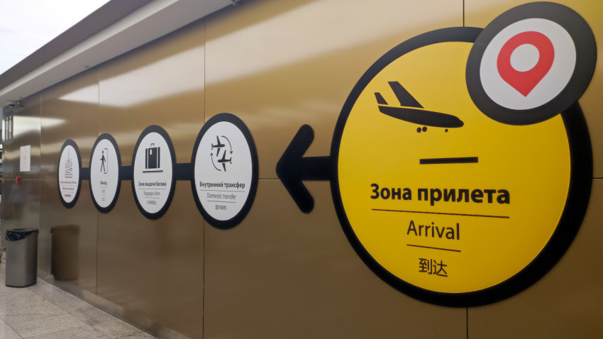 Табличка «Зона прилёта / Arrival» со стрелкой на стене терминала