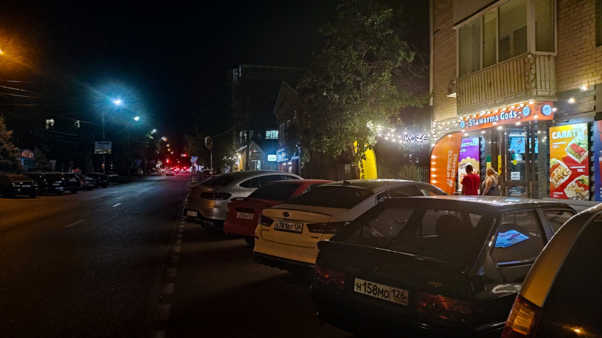 Ночная улица с припаркованными машинами и вывеской Shawarma Gods