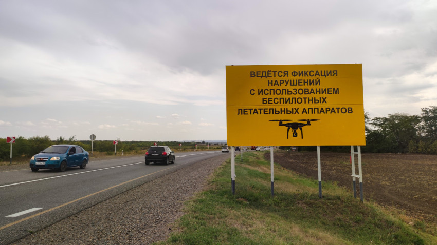 Жёлтый дорожный щит о фиксации нарушений ПДД с беспилотника у трассы