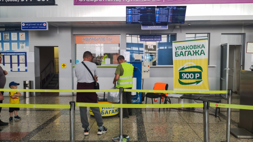 Зона упаковки багажа в аэропорту с ограждениями и рекламными баннерами