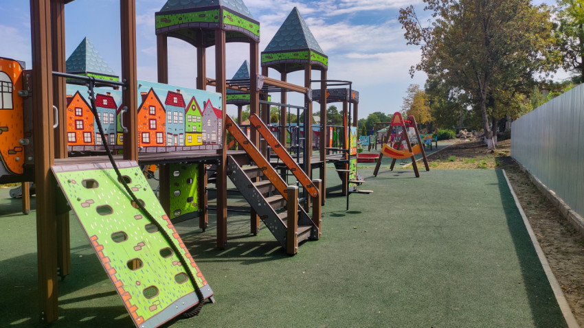 Общий вид детской площадки в посёлке с игровым городком и ограждением