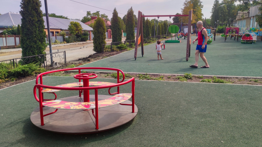 Детская площадка в поселке с каруселью и качелями
