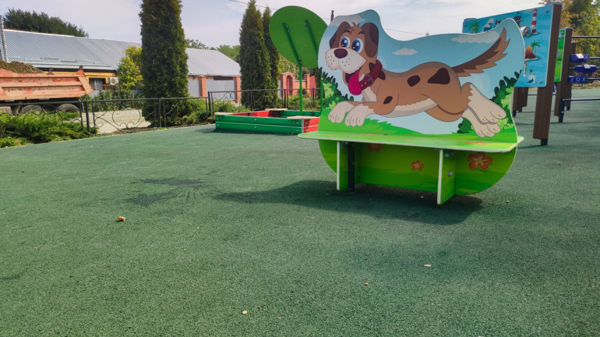 Лавочка с фигурой собаки на зелёном покрытии детской площадки