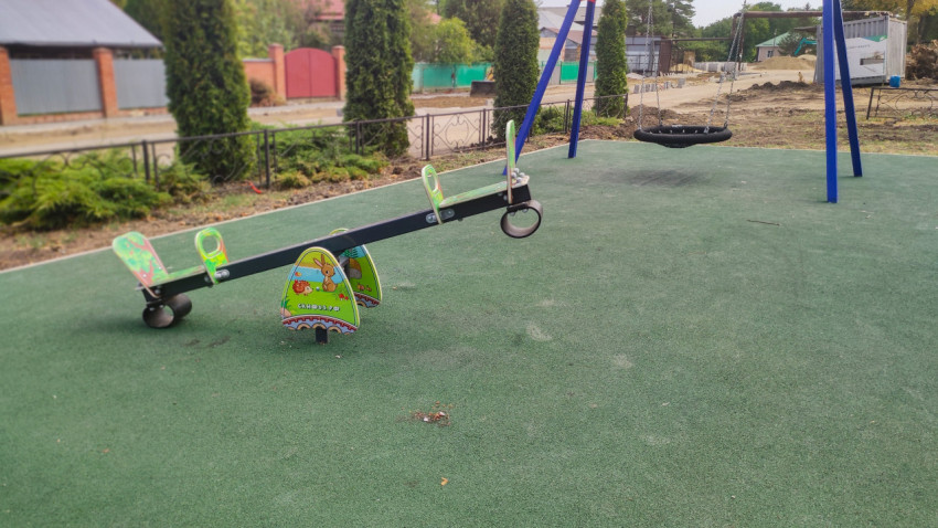 Балансир-качалка и качели-гнездо на зелёной площадке в посёлке