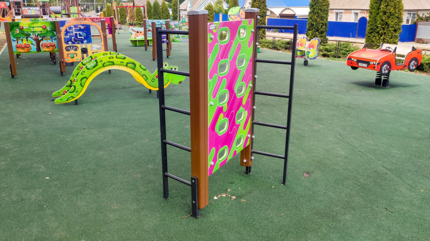 Игровой комплекс и качалка на зелёном резиновом покрытии во дворе