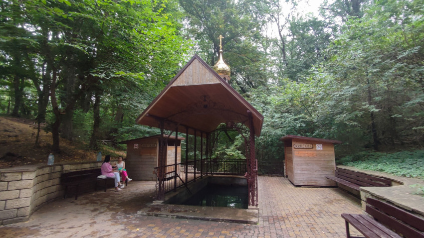 Навес над купелью святого источника среди леса и плиточной площадки