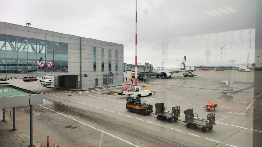 На перроне аэропорта тянется цепочка багажных тележек у самолёта и терминала