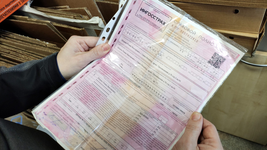 Человек держит в руке договор страхования автомобиля
