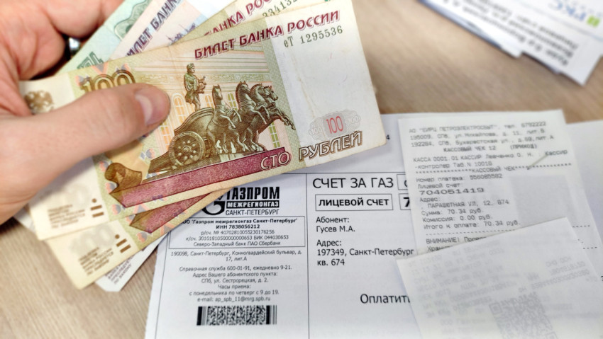 Рука, держащая стопку российских денег, на фоне счета за газ