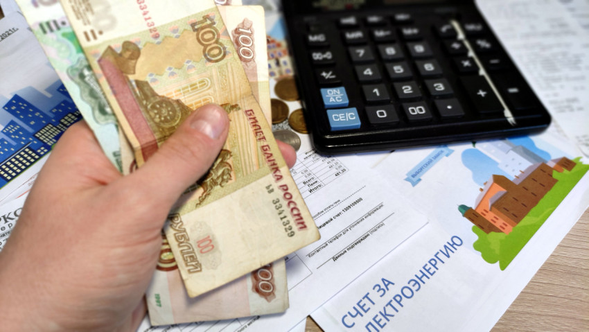 Человек держит пачку денег рядом с калькулятором и счетом за свет