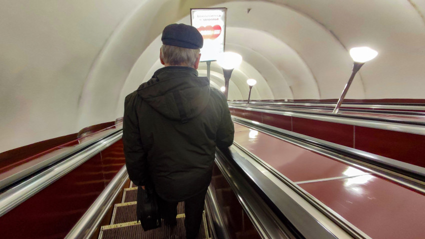 Пожилой мужчина спускается по эскалатору в метро