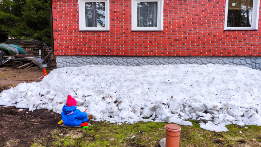 Ребёнок играет в снегу у дома