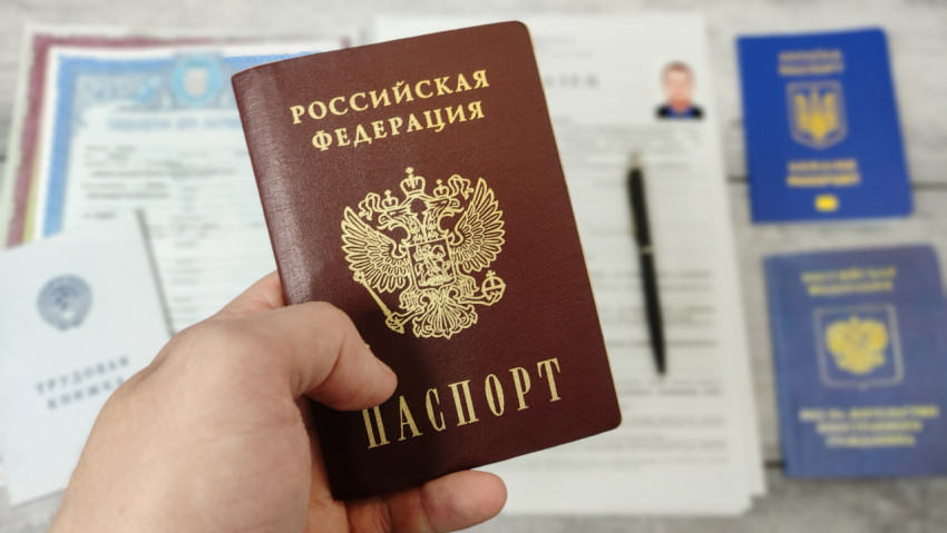 Паспорт гражданина РФ в руке на фоне трудовой книжки и документов
