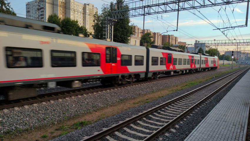 Уходящий пригородный поезд на фоне городской застройки