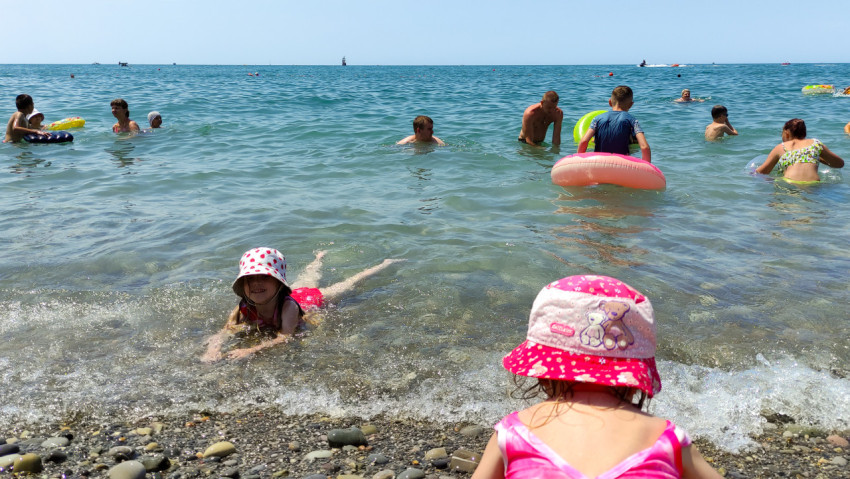 Дети играют у берега моря среди купающихся людей