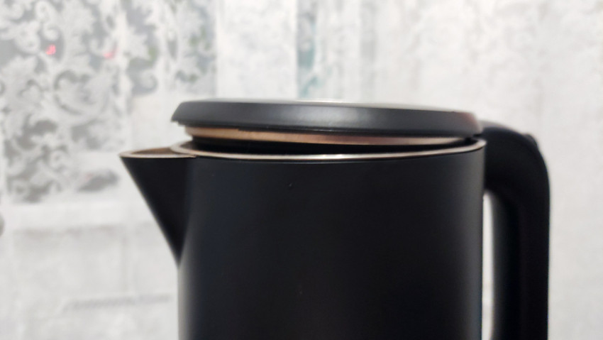 Чайник с приподнятой крышкой на кухонной поверхности