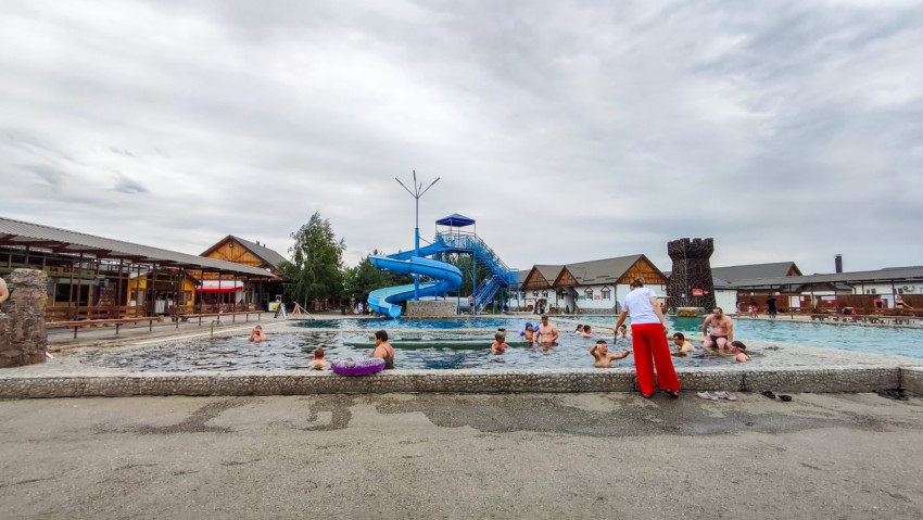 Панорама бассейна с водной горкой, павильонами и отдыхающими под пасмурным небом