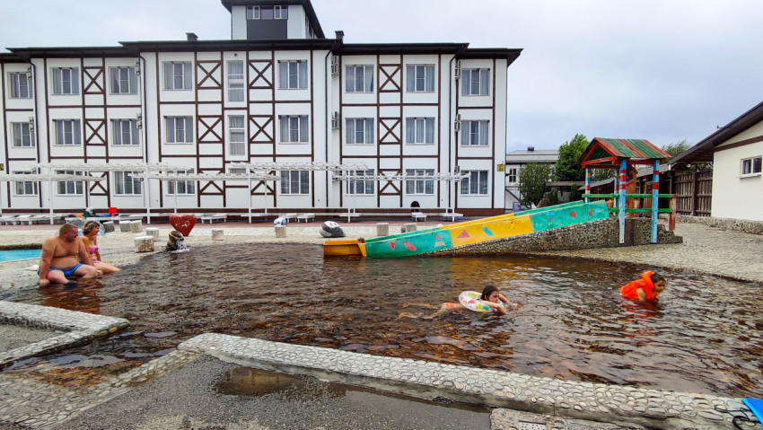 Мелкий бассейн с детьми и водной горкой на фоне гостиничного корпуса