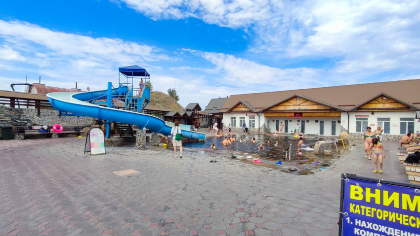 Панорама термального комплекса с бассейном, водной горкой и предупреждающим стендом