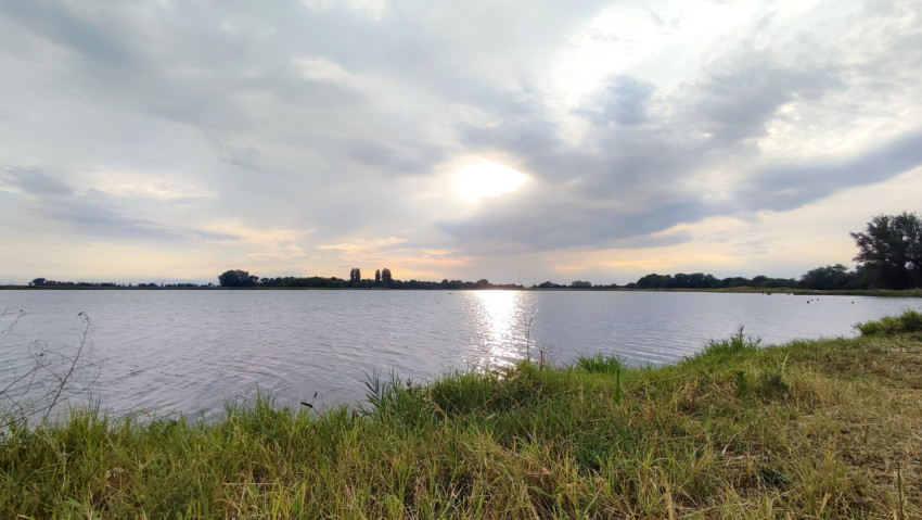 Берег водоёма с травой и мозаикой облаков в небе