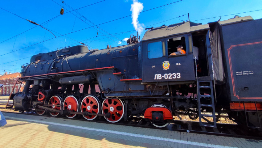 Паровоз ЛВ-0233 целиком сбоку на путях железнодорожной станции под контактной сетью